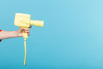 Photographing and vintage concept - female hand with yellow retro camera on blue background with copy space.