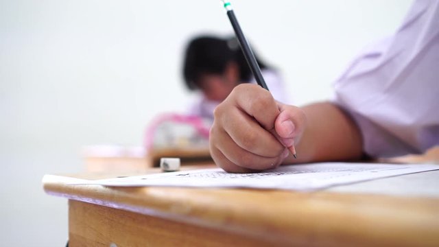 English exams test student in school, university students holding pencil for testing exam writing answer sheet or exercise for taking in assessment paper on table classroom. Education study Concept