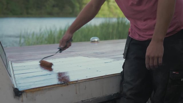 Youth rolling on exterior protective paint wooden boat roof