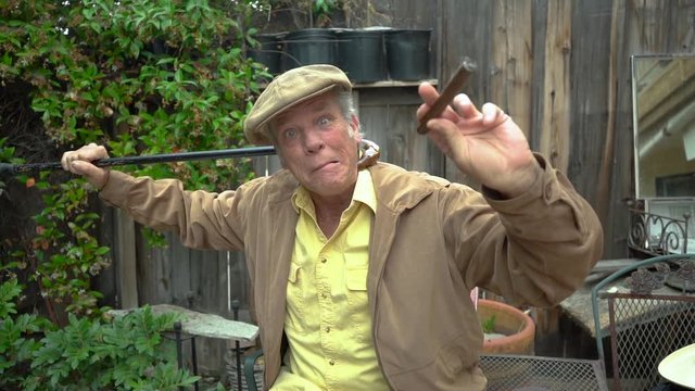 Silly and funny old man in his 60s being goofy with his cane and holding a cigar in his hand. Hilarious facial expressions, slow motion.