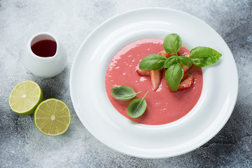 Cold summer strawberry soup served in a white plate, horizontal shot over grey stone background