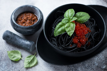 Spaghetti with squid-ink, red caviar and fresh green basil leaves, studio shot on a light-grey stone surface