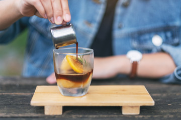 A woman pouring espresso shot into a glass of ice and lemon