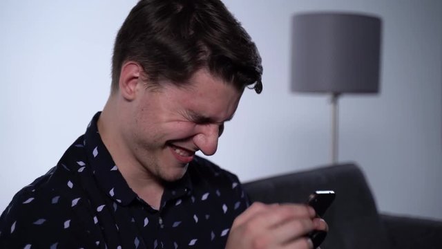 Caucasian Man Laughing at Phone in Apartment Living Room, Funny Text