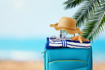 holidays. travel concept. blue suitcase with female hat, starfish, sunglasses and beach towel in...