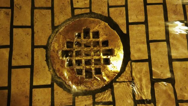 Medium close up shot of the drain of a fancy shower as the water spirals away.