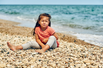 Beautiful little pensive girl on the sea coast . Children's summer holidays