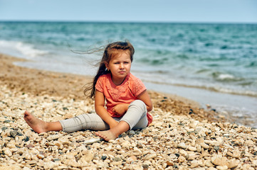 Fototapeta na wymiar Beautiful little pensive girl on the sea coast . Children's summer holidays