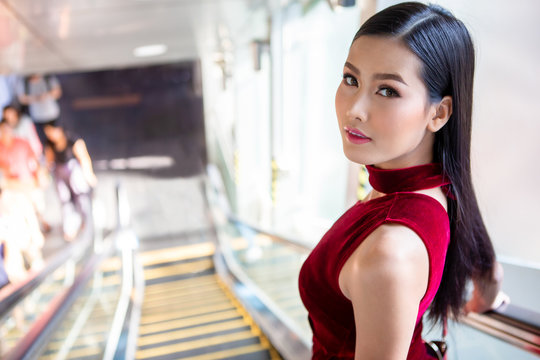 Beautiful young asian woman in red dress going down the escalator in shopping mall . happy elegant lady . copy space - Powered by Adobe