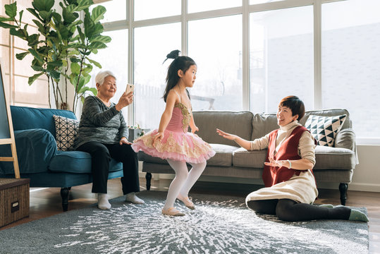 Senior woman taking photos for her dancing granddaughter at home