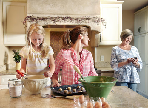 Three generations of women cooking together in the kitchen with grandma on the phone in the background - Powered by Adobe