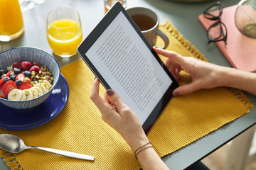 Woman reading ebook via tablet while having breakfast at home.