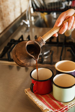 Hand pouring coffee from turk to enamel mugs
