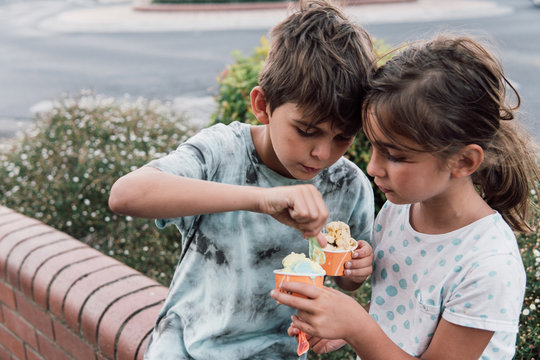 Brother and sister eating and sharing ice cream on the street