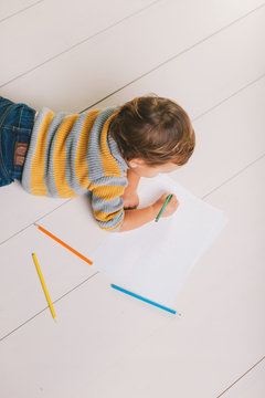 Overhead of cute child painting with color pencils on paper in the floor.