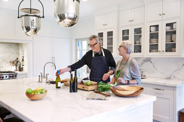 Mature couple with grey hair cooking in kitchen of luxury home
