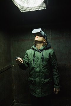 Young man using gray VR goggles finding himself in an industrial elevator