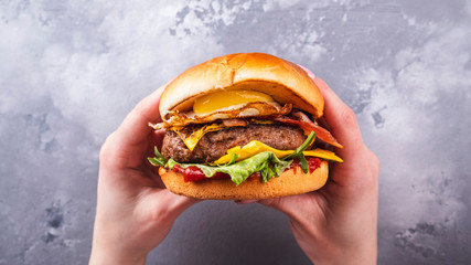 Female hands holding tasty beef burgers with fried egg and bacon. Top view