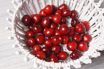 Red sweet cherries in a white basket on a white wooden table