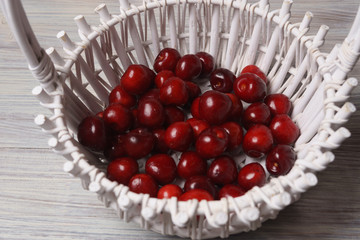 Red sweet cherries in a white basket on a white wooden table