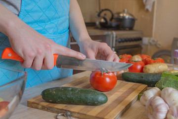 Chef cuts the vegetables into a meal. A woman uses a knife and cooks. Woman's hands cutting vegetables, behind fresh vegetables