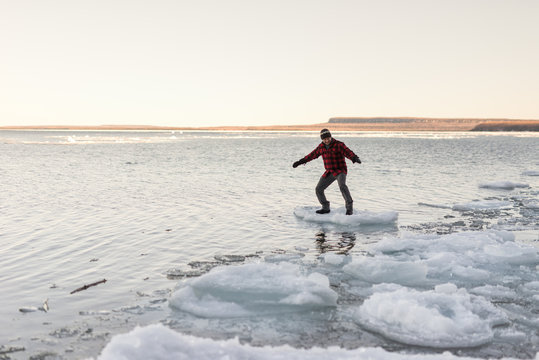 Man playfully balances and rides floating chunk of ice