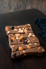 Bluberry Milk Chocolate Bar with Almond, Nuts and Raisin on Wooden Board.
