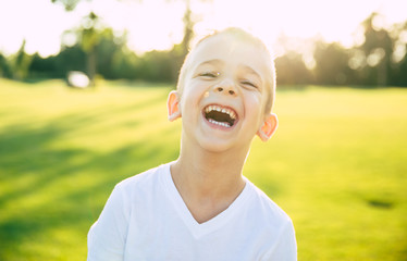 Close up portrait of beautiful happy and funny little boy or kid outdoors in green summer park