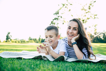 Happy family day. Beautiful lovely young mother with her cute little son is have a fun and hugging each other while lying on grass in park outdoors