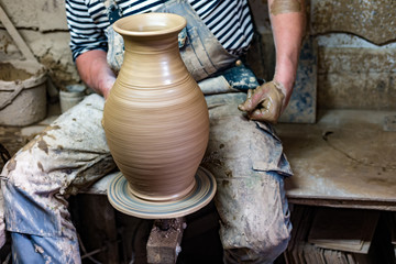 Craftsman in dirty clothes molding clay into desired shape on potter's wheel.
