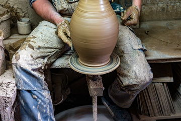 Craftsman in dirty clothes molding clay into desired shape on potter's wheel.
