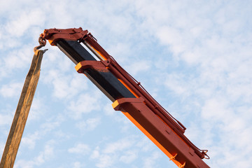 Red crane boom against the blue sky. Car manipulator unloads the pipe. Construction works. Summer....