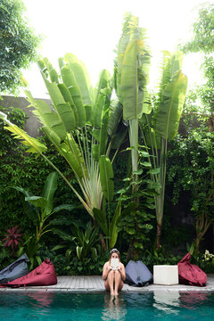 Relaxed sexy girl showing magazine sitting at the edge of a tropical pool.