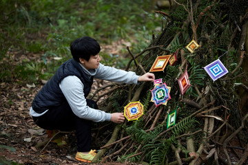 Asian female and her hand-woven dream catcher graphic in a natural wood environment.