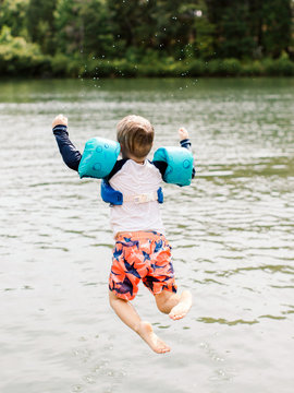 Little boy jumping into lake with swimmies on