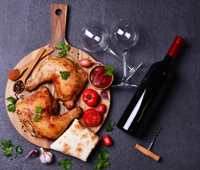 Grilled chicken drumsticks with spices and vegetables, with a bottle of red wine.