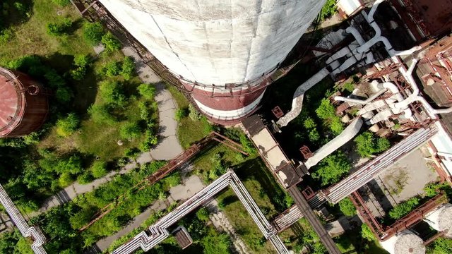 Top down aerial over abandoned and overgrown power station, following the contour downwards by chimney stack.