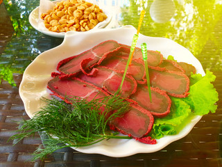 Delicious fresh basturma on a plate with lettuce and peanuts in a white saucer. Table in the summer...