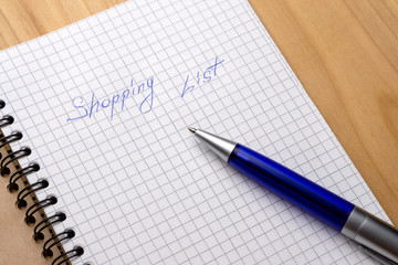 Blue pen on a notebook with sheets in a cage. Sign Shopping List