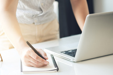 Young man is going to write the plan on blank notebook page and also working with laptop computer. Business startup concept.