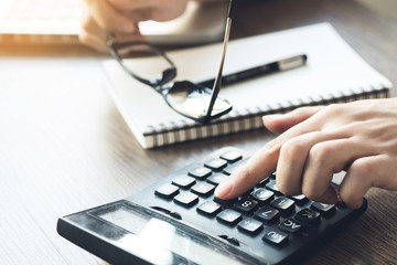 Business accountant man is using the calculator to calculate the income while holding the eye glasses because of stress. Calculate the financial cost concept.