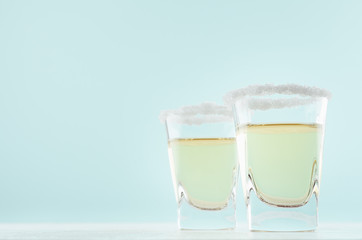 Fresh alcohol shot drink with tequila, salt rim on elegant pastel mint color background and white...