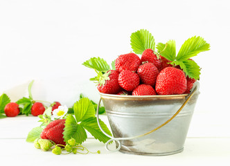 Juicy ripe tasty strawberries in  metal bucket on white wooden table.