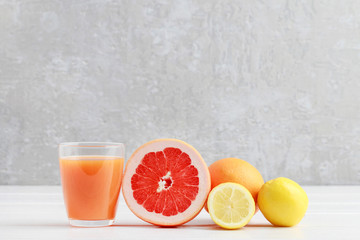 Glass of orange juice and juicy fruits on white wooden table.