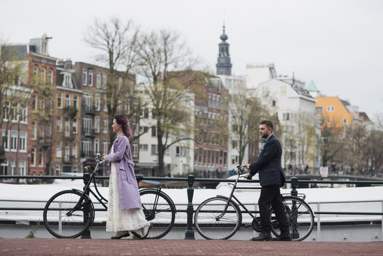 Wedding photo shooting. Bride and bridegroom walking in Amsterdam. Stand with bicycles near the canal