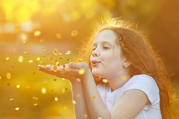 Little girl blowing gold confetti with her hand.