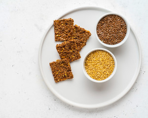 Golden and brown flax seeds and honey crackers on white stone background. Healthy raw vegan gluten free food concept.