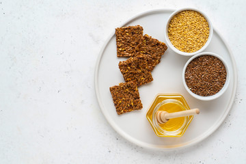 Golden and brown flax seeds and honey crackers on white stone background. Healthy raw vegan gluten free food concept.