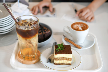 Barista is serving mixed coffee, latte and cake in a white tray.