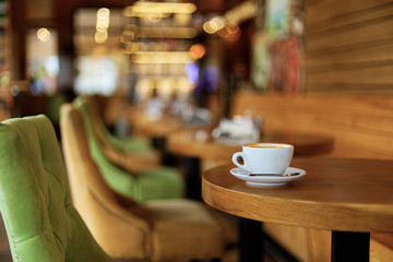 Cup of coffee cappuccino on a wooden table in a cafe. Shallow focus and lights on blurred background. Copyspace.